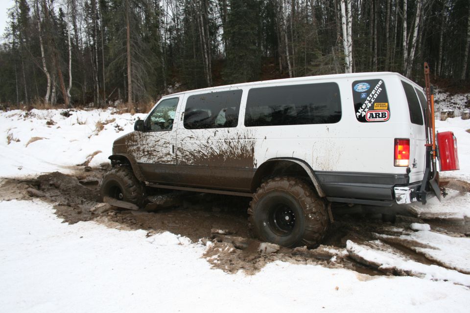 White van with off-road tires stuck in mud and snow, ARB sticker on rear window