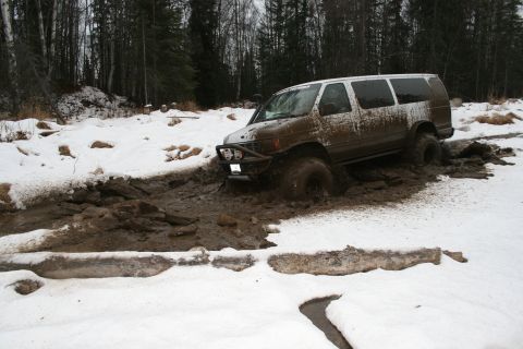 2003 Jeep TJ - A van is stuck in a muddy, snowy terrain, surrounded by trees.