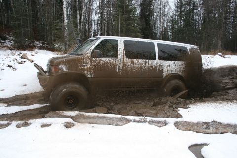 2003 Jeep TJ - A white van navigates a muddy trail in a snowy, wooded area, kicking up mud.