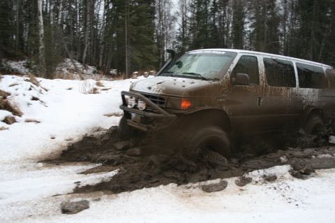 2003 Jeep TJ - A muddy van navigates a challenging off-road course through snow and deep mud, equipped with a snorkel and brush guard.
