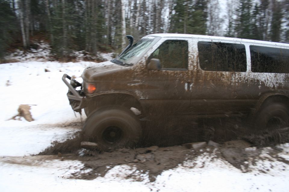 Mud-covered van with snorkel stuck in mud and snow, front wheel deep in mire