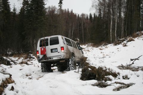 2003 Jeep TJ - A white van navigates a challenging snowy path through a dense forest.