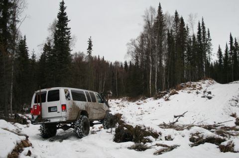 2003 Jeep TJ - Modified van navigates a snow-covered forest path with large off-road tires.