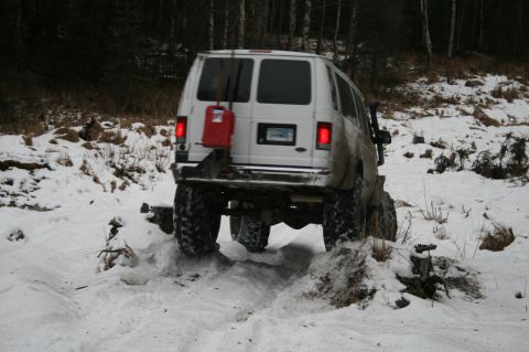 2003 Jeep TJ - White van with large off-road tires driving through snow, a red gas can is mounted on the rear door.