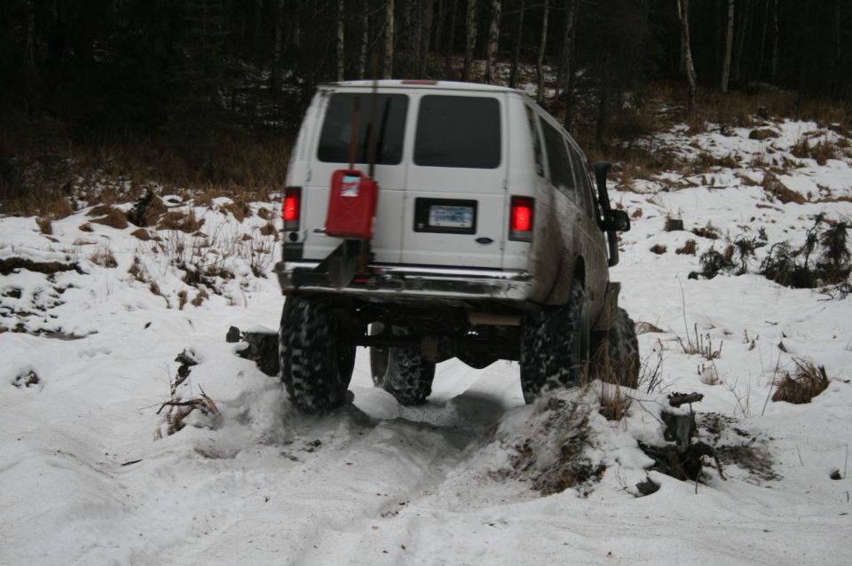 White van with off-road tires navigating a snowy trail, red gas can mounted on rear