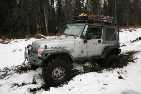 2003 Jeep TJ - A silver Jeep Wrangler Rubicon is stuck in the mud and snow, with its tires partially submerged.