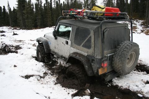 2003 Jeep TJ - A white Jeep Wrangler is stuck in a muddy, snowy terrain, its tires deep in the mire.