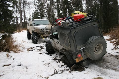2003 Jeep TJ - Two off-road vehicles navigate a snowy, muddy trail with one Jeep TJ stuck in the mire.