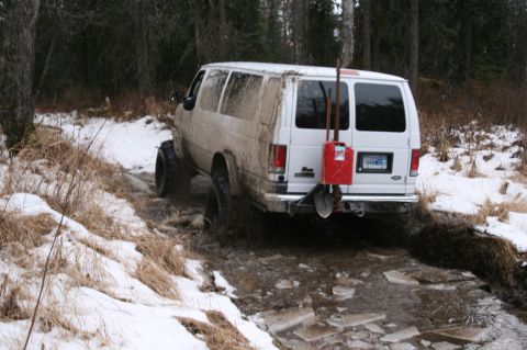 2003 Jeep TJ - A white van navigates a muddy, icy trail in a wooded area during winter.