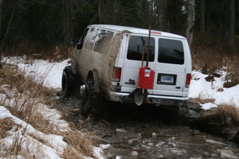2003 Jeep TJ - A white van equipped with off-road tires navigates a challenging snowy and muddy terrain.