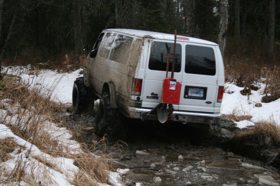White van with off-road tires navigating a muddy, snowy trail