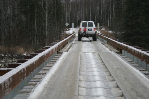 2003 Jeep TJ - A white van travels across a bridge covered in snow and ice, with a forest lining the sides.
