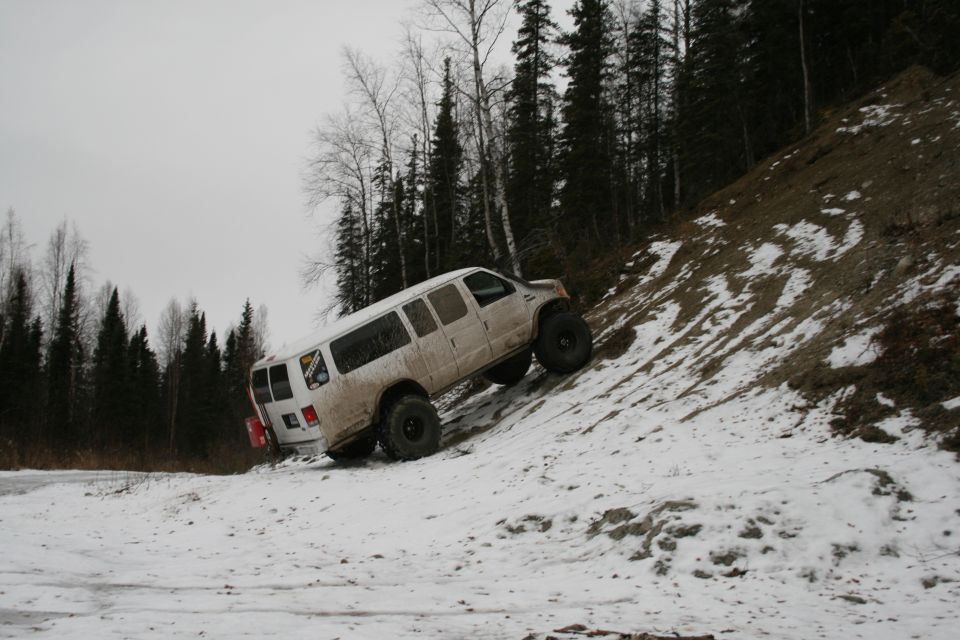 White van with large tires climbing a snowy hill, two vehicles visible