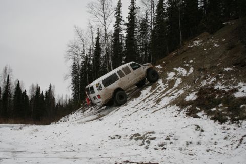 2003 Jeep TJ - A white van navigates a steep, snow-dusted embankment with a dense forest in the background.