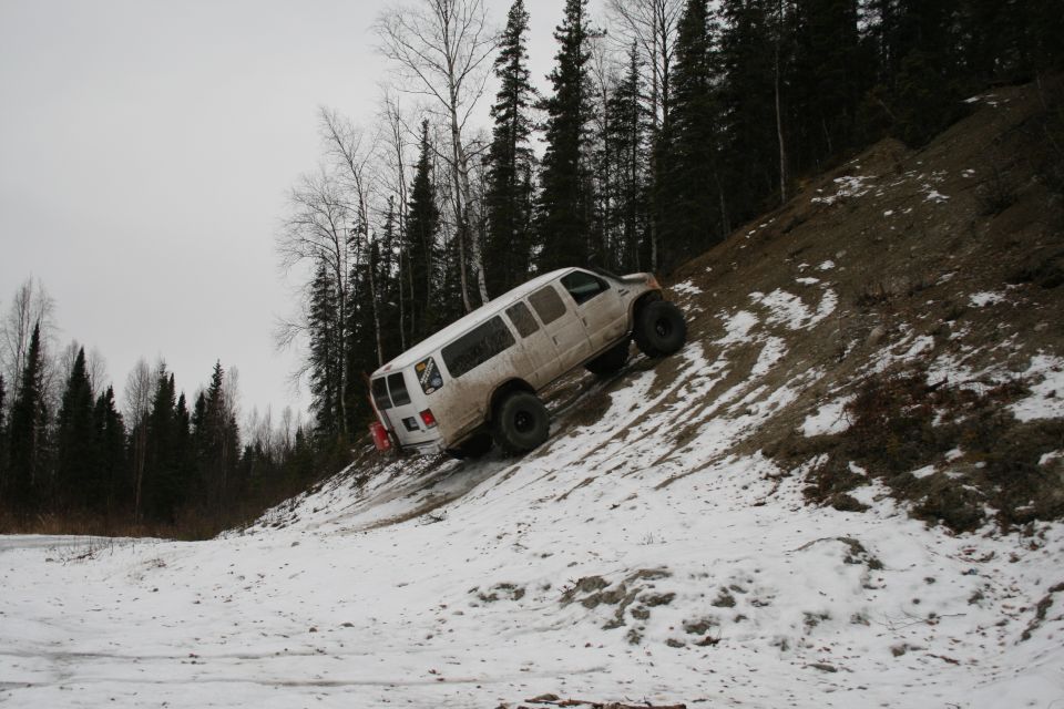White van with large tires climbing a snowy hill next to a forest