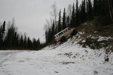 2003 Jeep TJ - A white van navigates a challenging snowy incline, surrounded by a dense forest.