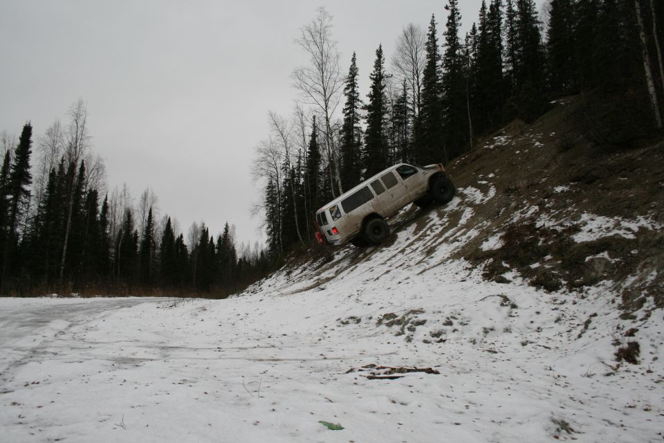 White van driving up a steep, snowy hill next to a forest
