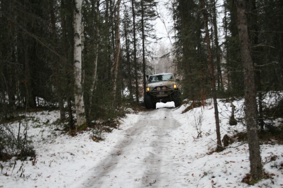 Tan Jeep TJ driving on a snow-covered dirt road through a forest