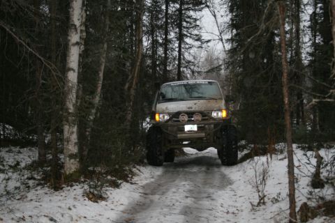 2003 Jeep TJ - A modified van navigates a snowy forest road, its large tires suited for off-road conditions.