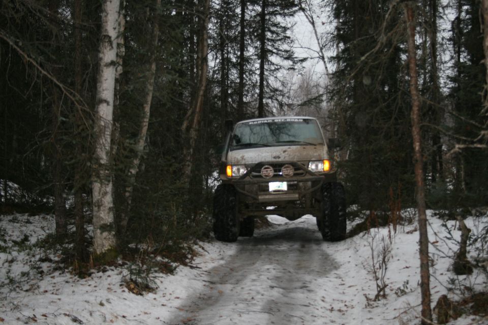 Modified van with large tires driving on a snowy path through a forest