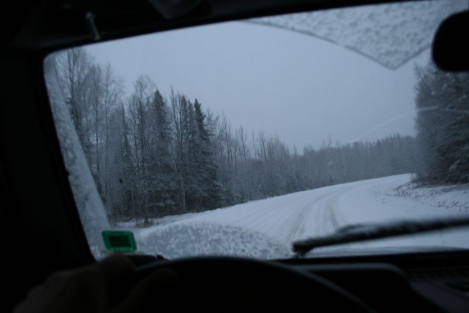 Interior view of a snowy road through a windshield with trees lining the sides
