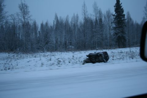 2003 Jeep TJ - A large rock rests on a snow-covered embankment beside a road, with a dense forest of bare trees behind it.