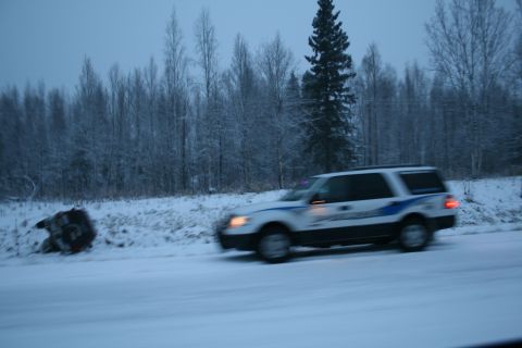 2003 Jeep TJ - A white SUV with a blue stripe drives past a snow-covered ditch on a winter day.