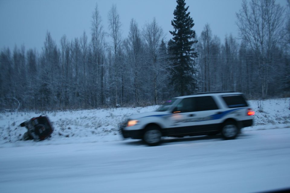 White SUV with blue stripe driving on snowy road