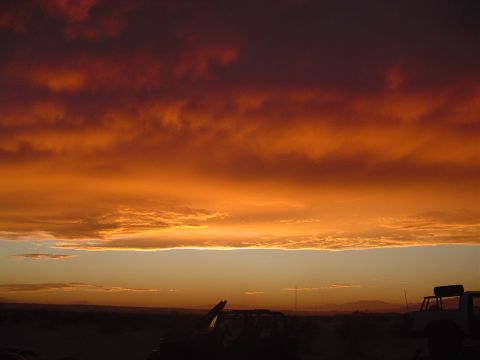 2000 Jeep TJ - The sky is ablaze with color during a desert sunset, with the shapes of vehicles barely visible below.