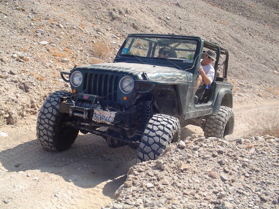 Green Jeep Wrangler with big tires driving on a dirt trail with rocky hills