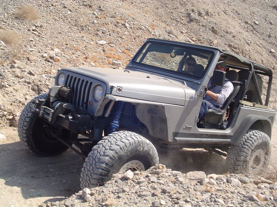 Gray Jeep Wrangler TJ driving on a rocky trail, front passenger side tire is lifted