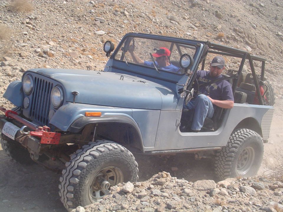 Blue Jeep CJ-7 with off-road tires navigating rocky terrain