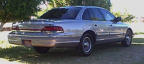 1994 Ford Crown Victoria - Rear view of a 1994 Ford Crown Victoria sedan parked on grass with trees in the background.