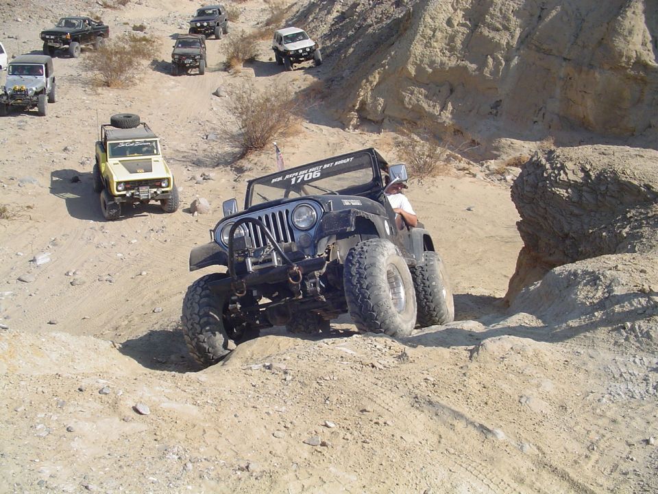 Black Jeep Wrangler with large tires navigating a rocky, sandy trail