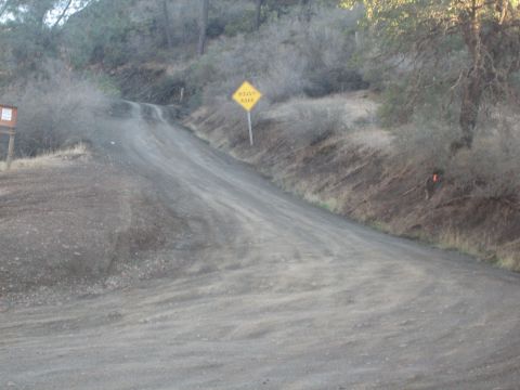 1995 Ford Bronco - A dirt road winds uphill through a dry, wooded area, marked by a "ROUGH ROAD" sign.