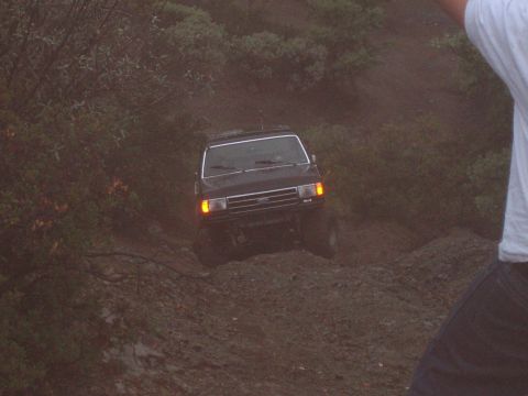 1995 Ford Bronco - A dark-colored Ford Bronco navigates a steep, muddy incline with vegetation on either side.