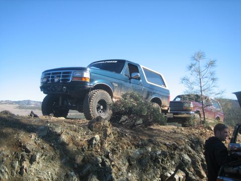 1995 Ford Bronco - Two off-road vehicles are parked on a rocky hill with a clear blue sky above.