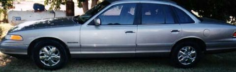 1994 Ford Crown Victoria - A silver sedan with tinted windows is parked outdoors on a grassy area.