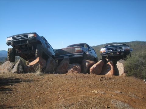 1995 Ford Bronco - Multiple Ford Broncos navigate a rocky obstacle course under a clear blue sky.