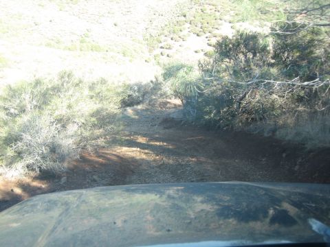 1995 Ford Bronco - A view from inside a vehicle looking out at a dirt road winding through a dry, brush-filled landscape.