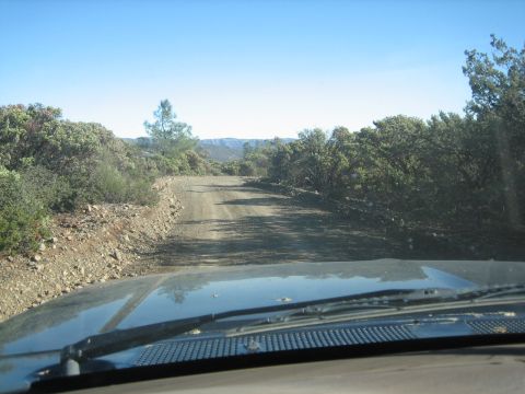1995 Ford Bronco - View from inside a vehicle driving on a dusty, winding dirt road through a rural, arid landscape.