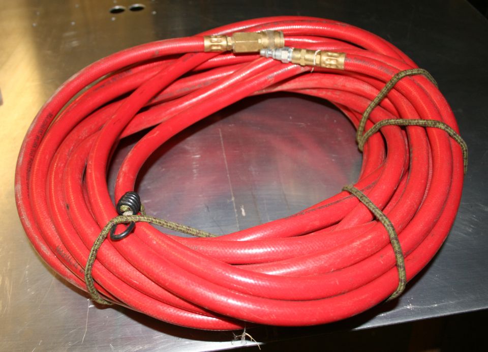 Coiled red air hose with brass quick-connect fittings and a dark green tie-down strap