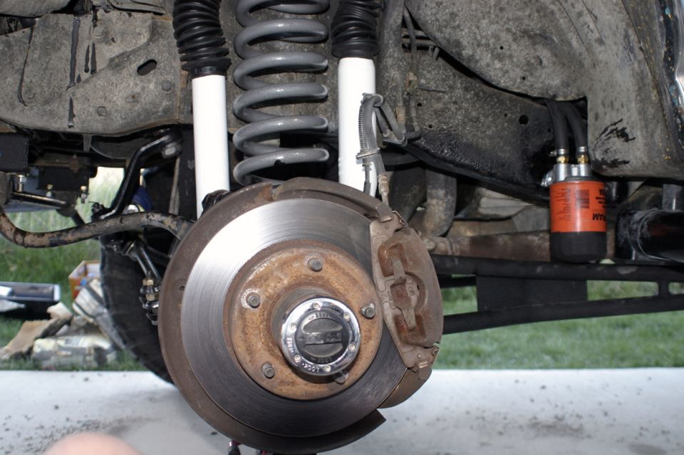 Front brake rotor, locking hub, coil spring and dual shocks with wheel removed on a lifted 1994 Ford Bronco