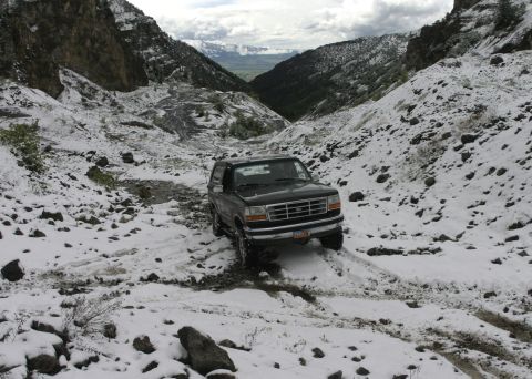 1994 Ford Bronco - A black 1994 Ford Bronco navigates a snow-covered mountain trail, its off-road capability.