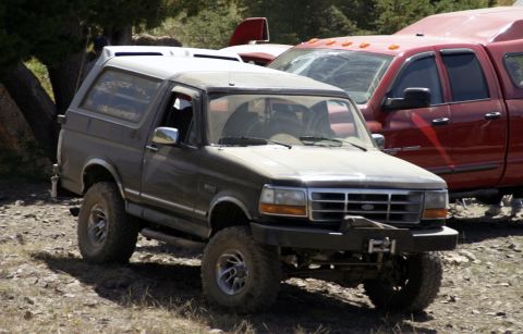 1994 Ford Bronco - Ford Bronco SUV parked off-road with a red pickup truck in the background.