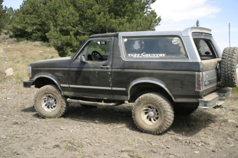 1994 Ford Bronco - This lifted Ford Bronco is parked off-road with a spare tire mounted on the rear tailgate.