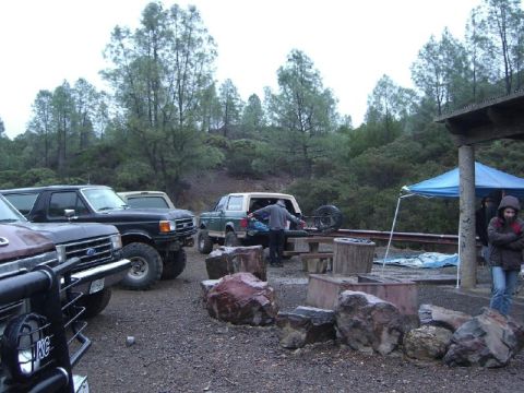 1989 Ford Bronco - Multiple Ford Broncos are gathered at a campsite, with people and camping gear visible.