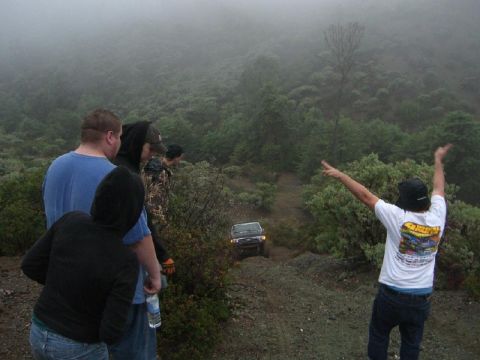 1989 Ford Bronco - A 1989 Ford Bronco navigates a steep, foggy trail as onlookers watch from above.