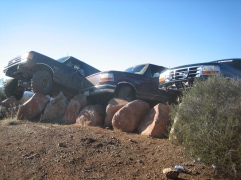 1989 Ford Bronco - Three trucks are shown navigating a rocky terrain under a clear blue sky.