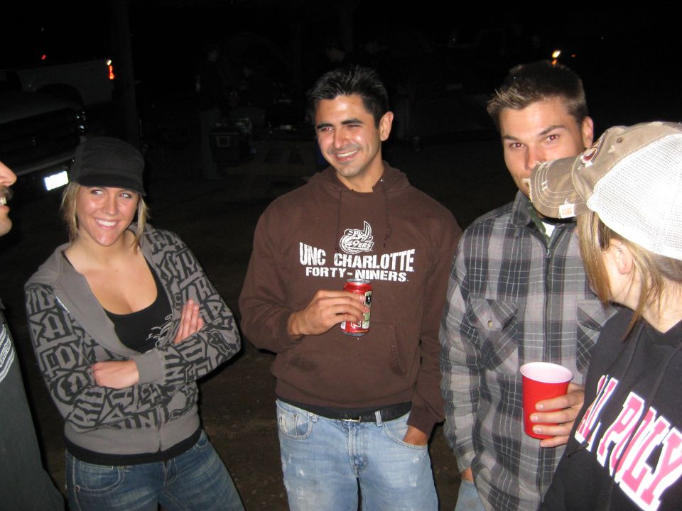 People gathered at night, one man wears a UNC Charlotte hoodie, another a plaid shirt